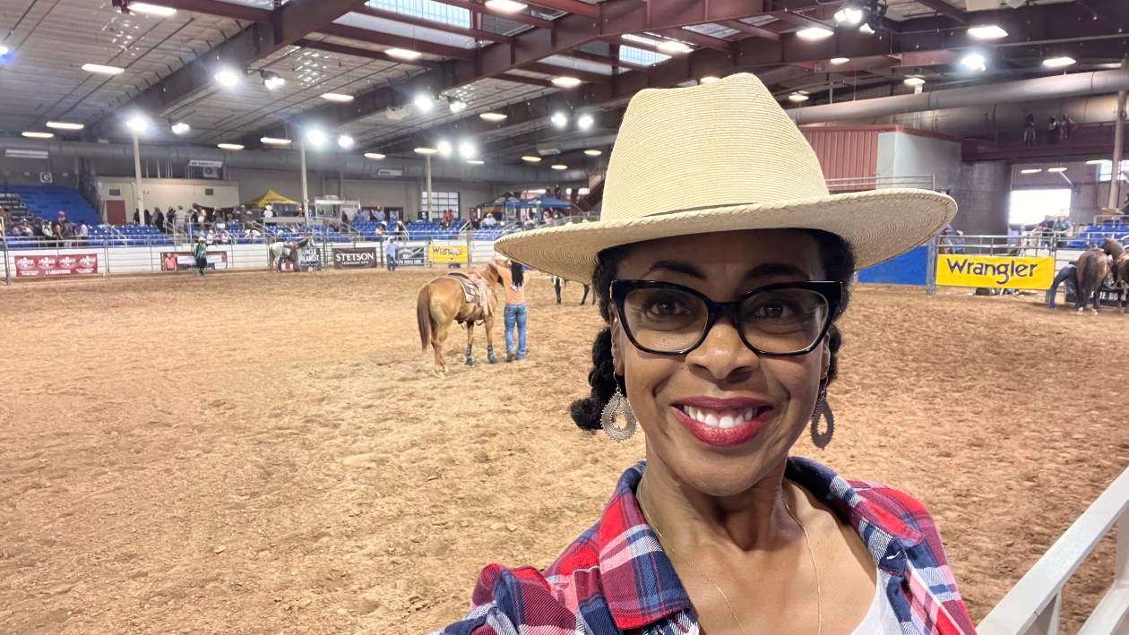 Woman in cowboy hat with rodeo ring behind her